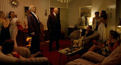 Still from Bronson (2008) that has been tagged with: group-shot & wide shot & fireplace & living room & practical lamp & party