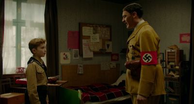Still from JoJo Rabbit (2019) that has been tagged with: day & swastika & medium wide & profile shot & interior & hitler