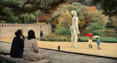 Still from Past Lives (2023) that has been tagged with: group-shot & day & exterior & park bench